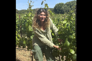 Bäuerin mit langen Haaren steht bei den Weinreben.