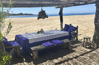 Gedeckter Holztisch am Strand mit Blick aufs Meer.