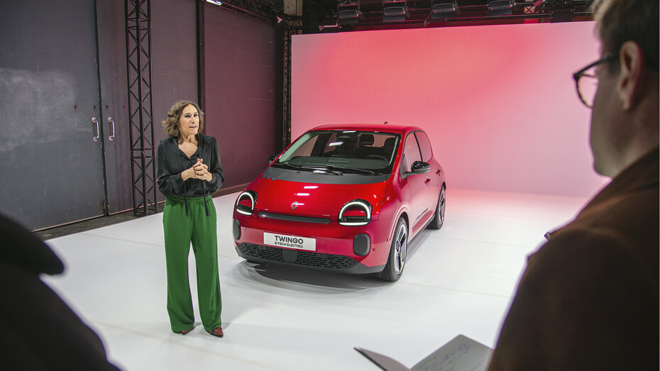Eine Frau steht vor einem roten Renault Twingo 2025, der in einem Studio steht.