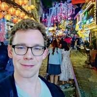 Ein junger Mann mit Brille macht ein Selfie in einer Gasse mit Zugschienen