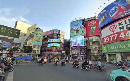 Viele Roller fahren auf einer Straße vor Häusern voller Reklame.