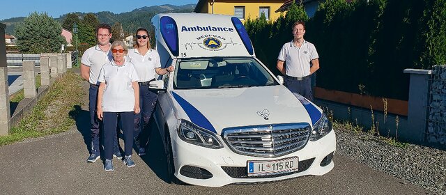 ÖAMTC-Clubmitglieder stehen gemeinsam mit Sanitätern vor einem Krankenfahrzeug.