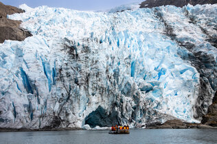 Zodiac mit 12 Schwimmwesten tragenden Passagieren vor der türkis-weißen Eis-Front des Condor-Gletschers