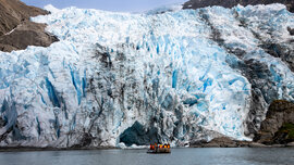 Zodiac mit 12 Schwimmwesten tragenden Passagieren vor der türkis-weißen Eis-Front des Condor-Gletschers