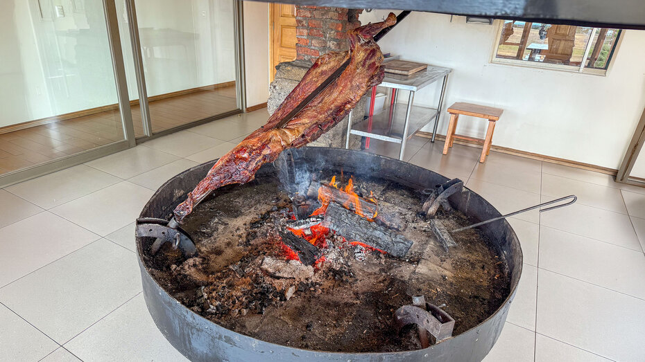 Asador-Grill mit einem halben Lamm auf einem schräg über dem Feuer steckenden Spieß
