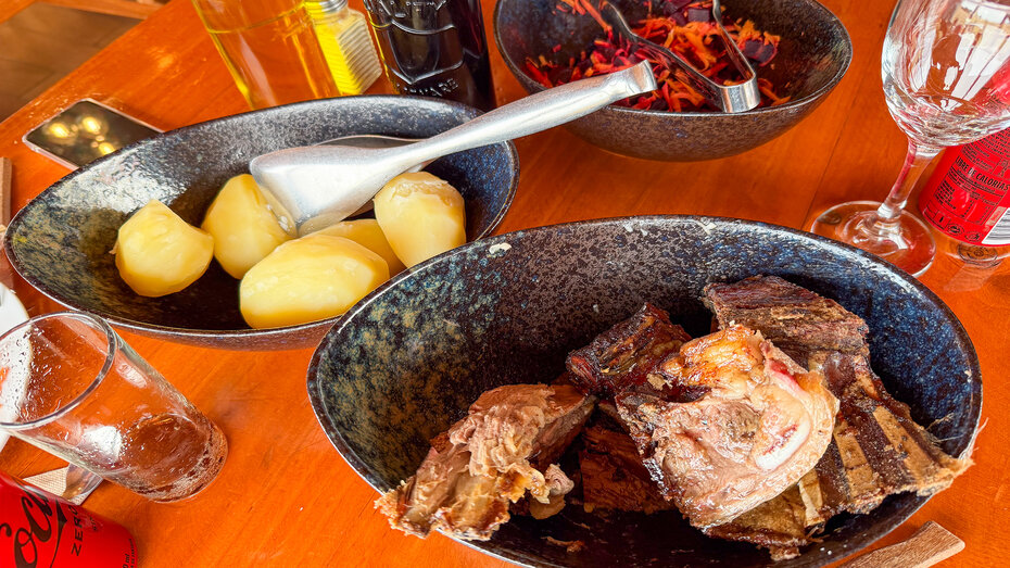 Tisch mit drei Tellern mit Lammfleisch, Salzkartoffeln und Karotten-/Rübensalat