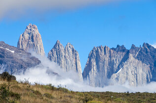 Gebirgskette mit den Torres del Paine in der Sonne, davor Wolken und Nebelfetzen