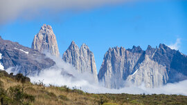Gebirgskette mit den Torres del Paine in der Sonne, davor Wolken und Nebelfetzen