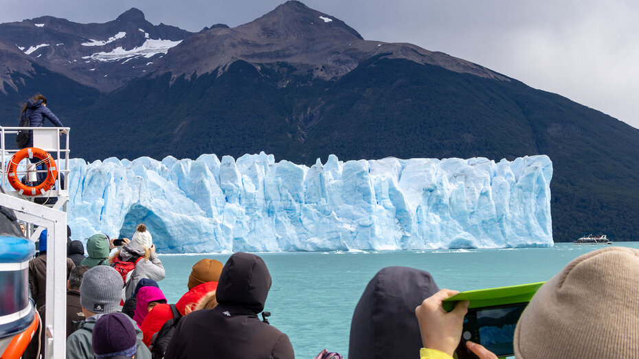 Die hellblau-türkis schimmernde Front des Perito-Moreno-Gletscher vom Schiff aus gesehen, im vordergrund Touristen, die fotografieren