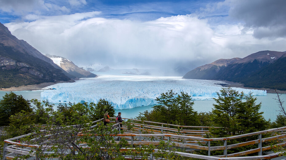 Weiß-Hellblauer Perito Moreno-Gletscher vom Gegenhang aus gesehen, dahinter die wolkenverhangenen Zweieinhalbtausender