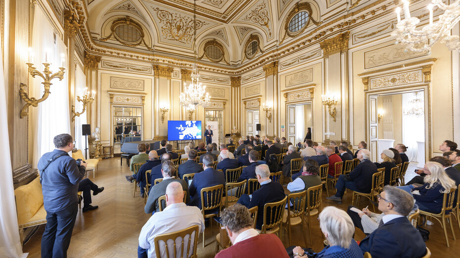 Eine Pressekonferenz findet in einem Saal voller Journalisten statt.