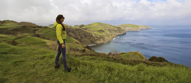 Eine Dame steht an der grünen Küste von Sao Miguel und schaut aufs Meer.
