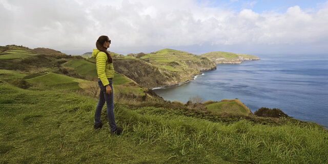  Eine Dame steht an der grünen Küste von Sao Miguel und schaut aufs Meer.