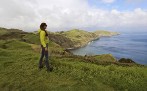  Eine Dame steht an der grünen Küste von Sao Miguel und schaut aufs Meer.