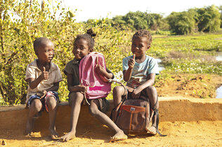 Drei Kinder sitzen mit ihrem Rucksack.