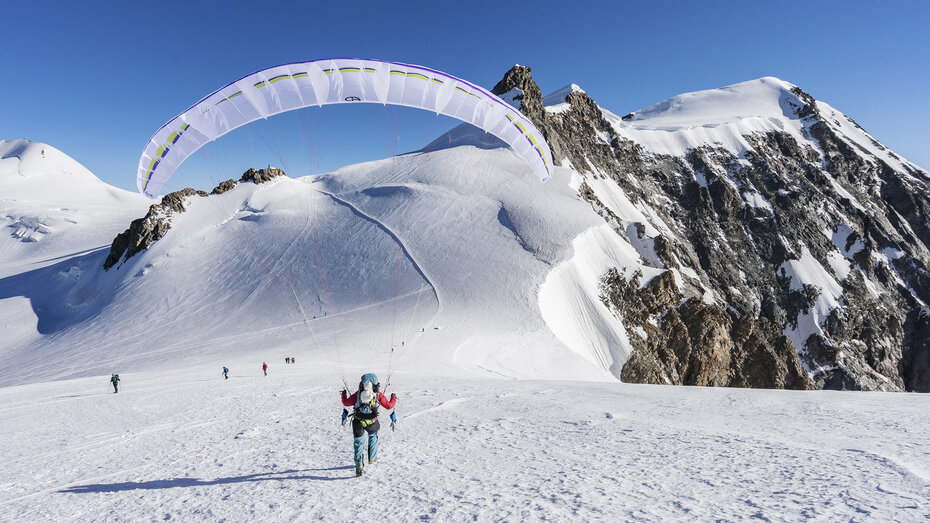 Auf der Vincentpyramide mit dem Gleitschirm landet jemand auf einer schneebedeckten Landebahn, Berge im Hintergrund.