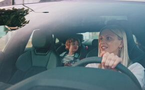 Eine blonde Frau am Steuer eines Autos, am Rücksitz sitzt ein Kind.