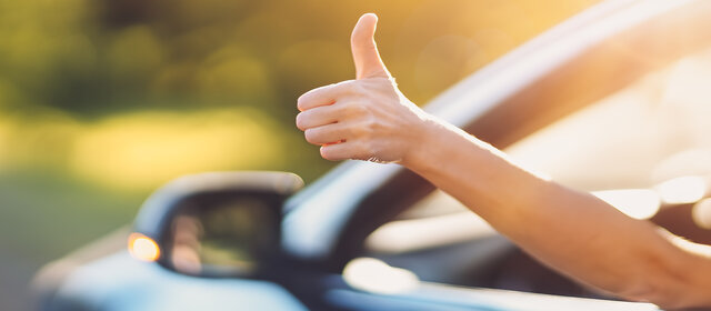 Eine Hand ragt aus einem offenen Autofenster und gibt Daumen hoch.