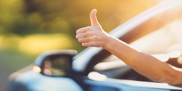 Eine Hand ragt aus einem offenen Autofenster und gibt Daumen hoch.