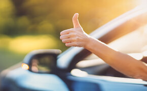 Eine Hand ragt aus einem offenen Autofenster und gibt Daumen hoch.