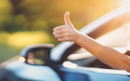 Eine Hand ragt aus einem offenen Autofenster und gibt Daumen hoch.