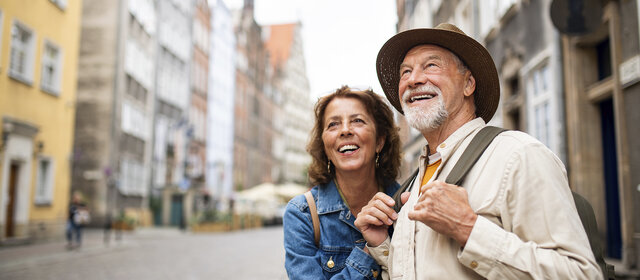 Porträt eines glücklichen Seniorenpaares, das als Touristen im Freien in einer historischen Altstadt unterwegs ist.