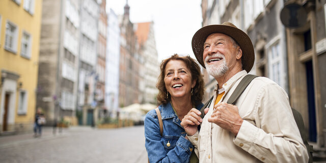 Porträt eines glücklichen Seniorenpaares, das als Touristen im Freien in einer historischen Altstadt unterwegs ist.