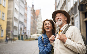 Porträt eines glücklichen Seniorenpaares, das als Touristen im Freien in einer historischen Altstadt unterwegs ist.