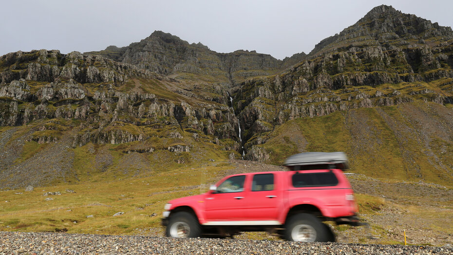 Ein rotes Auto fährt entlang einer spektakulären Felslandschaft.