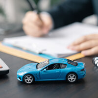 Ein blaues Modellauto steht auf einem Tisch neben einem Rechner und einem Block