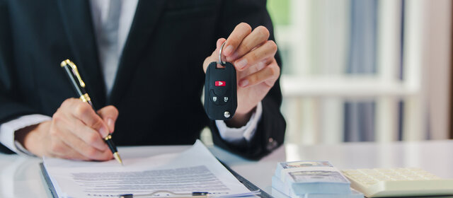 Jemand unterschreibt etwas und hält mit der anderen Hand einen Autoschlüssel