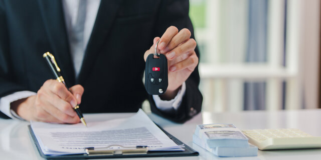 Jemand unterschreibt etwas und hält mit der anderen Hand einen Autoschlüssel