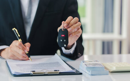 Jemand unterschreibt etwas und hält mit der anderen Hand einen Autoschlüssel