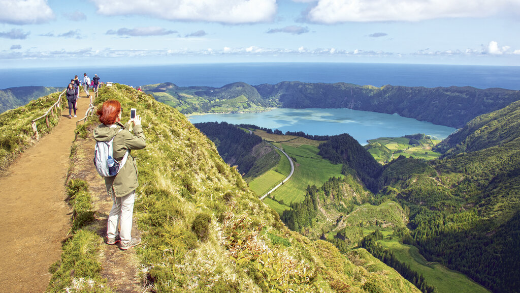 Specktakulärer Blick vom Vulkankrater auf auf den Vulkansee. Eine Frau fotografiert den Vulkansee mit dem Handy.