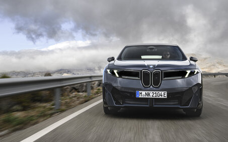 Ein dunkelgrauer BMW iX3 fährt auf einer Landstraße.