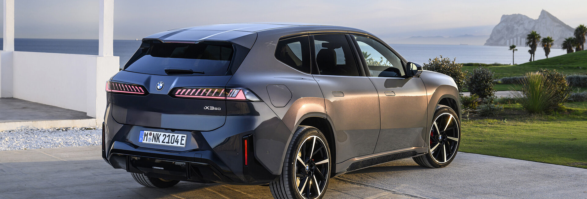 Ein BMW iX3 steht neben einem weißen Gebäude, hinter dem sich das Meer befindet.