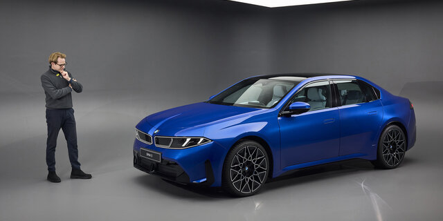 Eine Person steht in einem Studio links neben einer blauen BMW i3 Limousine.