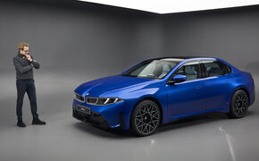 Eine Person steht in einem Studio links neben einer blauen BMW i3 Limousine.