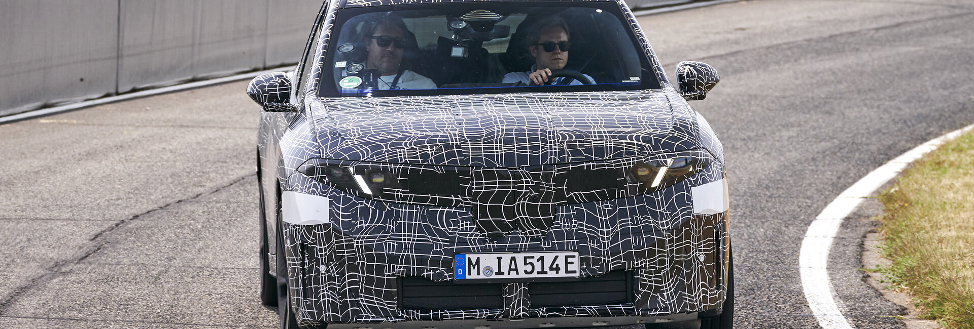 Ein getarnter BMW iX3 fährt durch eine Steilwandkurve.