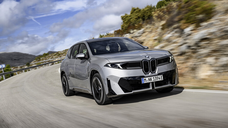 Ein BMW iX3 fährt durch eine Kurve auf einer Landstraße. 