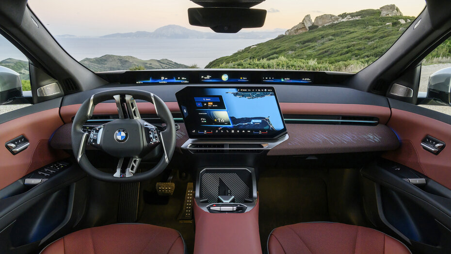 Innenraum eines BMW iX3 mit großem Touchscreen, Panoramic Vision und roten Materialien.