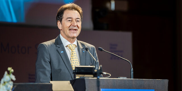 Ein Mann im Anzug mit gelber Krawatte spricht an einem Rednerpult