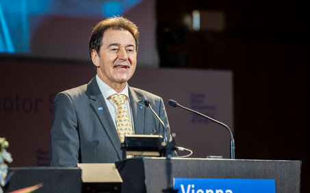 Ein Mann im Anzug mit gelber Krawatte spricht an einem Rednerpult