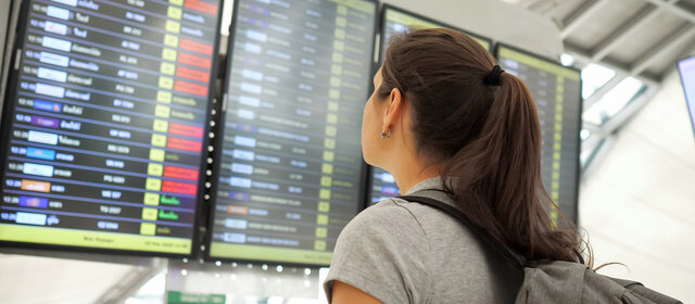 Ein Fluggast steht vor der Tafel am Flughafen und schaut wann ihr Flug abfliegt.