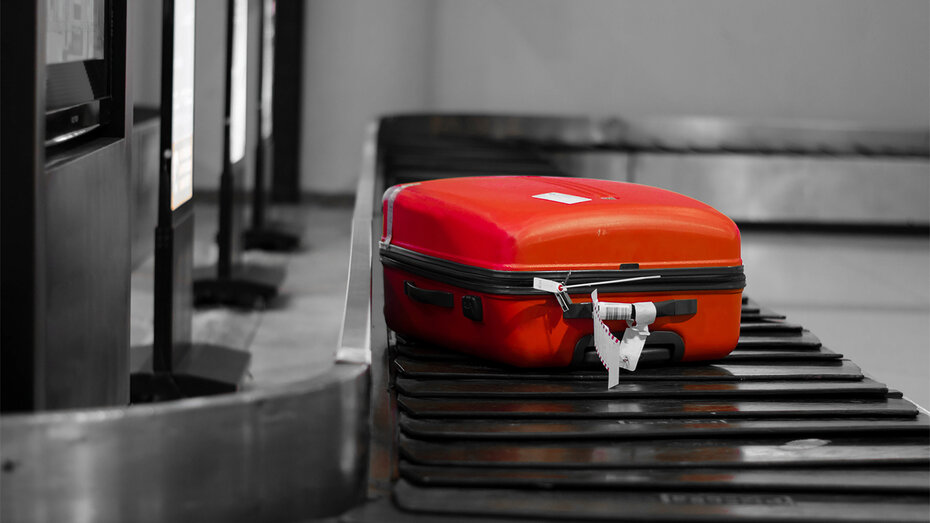 Ein roter Koffer liegt auf dem Kofferförderband am Flughafen.