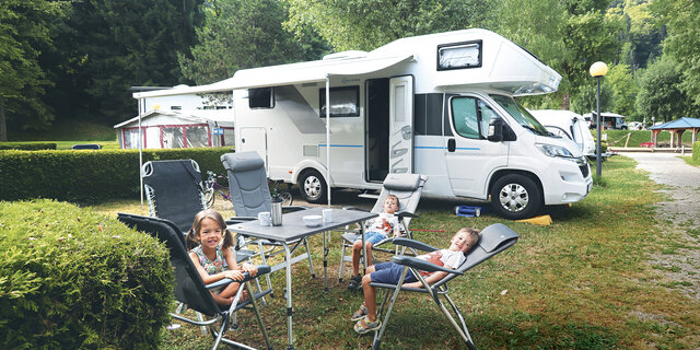 Drei kleine Kinder sitzen am Tisch vor ihrem Wohnmobil.