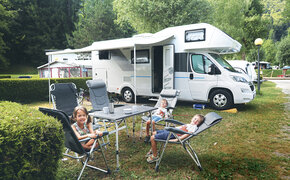 Drei kleine Kinder sitzen am Tisch vor ihrem Wohnmobil.