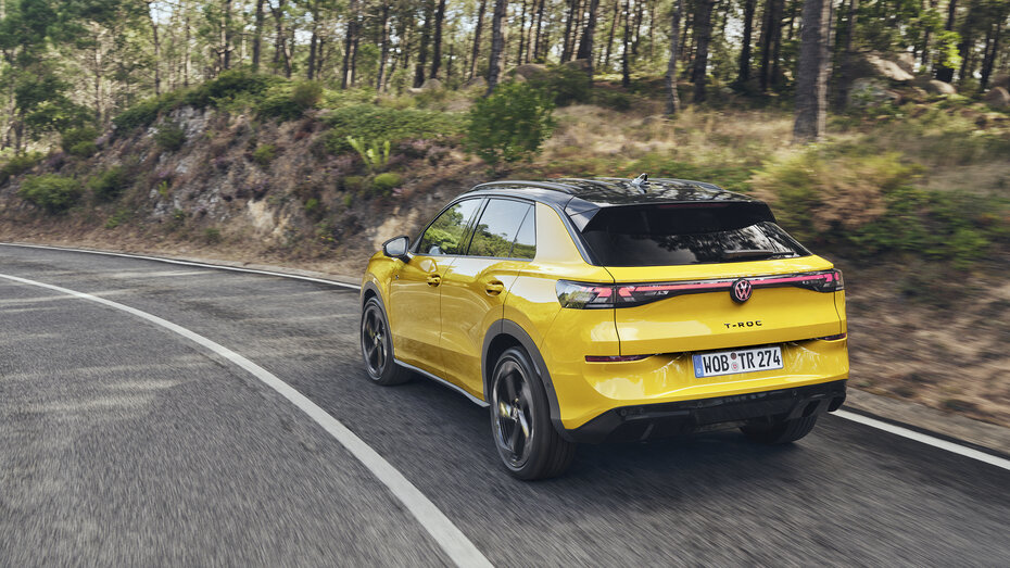 Ein gelber VW T-Roc fährt über eine Landstraße im Wald.