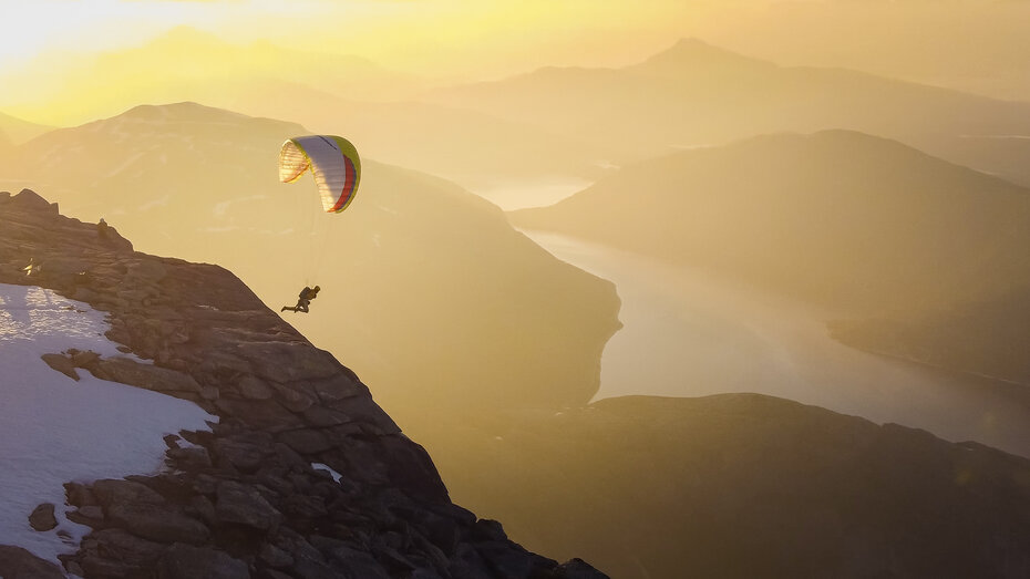 Gleitschirm, der über in Sonnenlicht getauchte Berge fliegt.