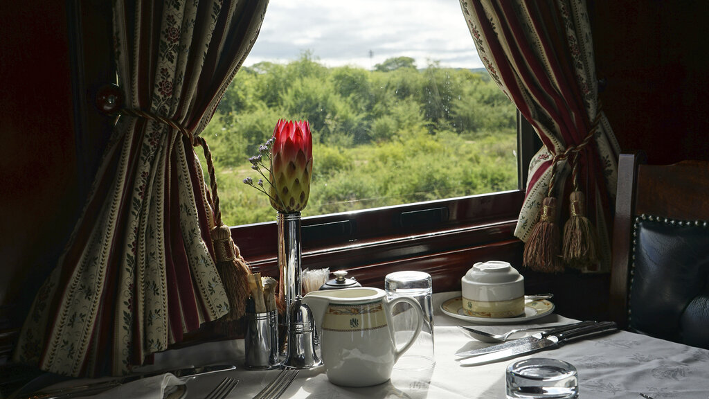 Frühstücksgeschirr am Fenstertisch, dazu eine rote Blume in einer Vase.